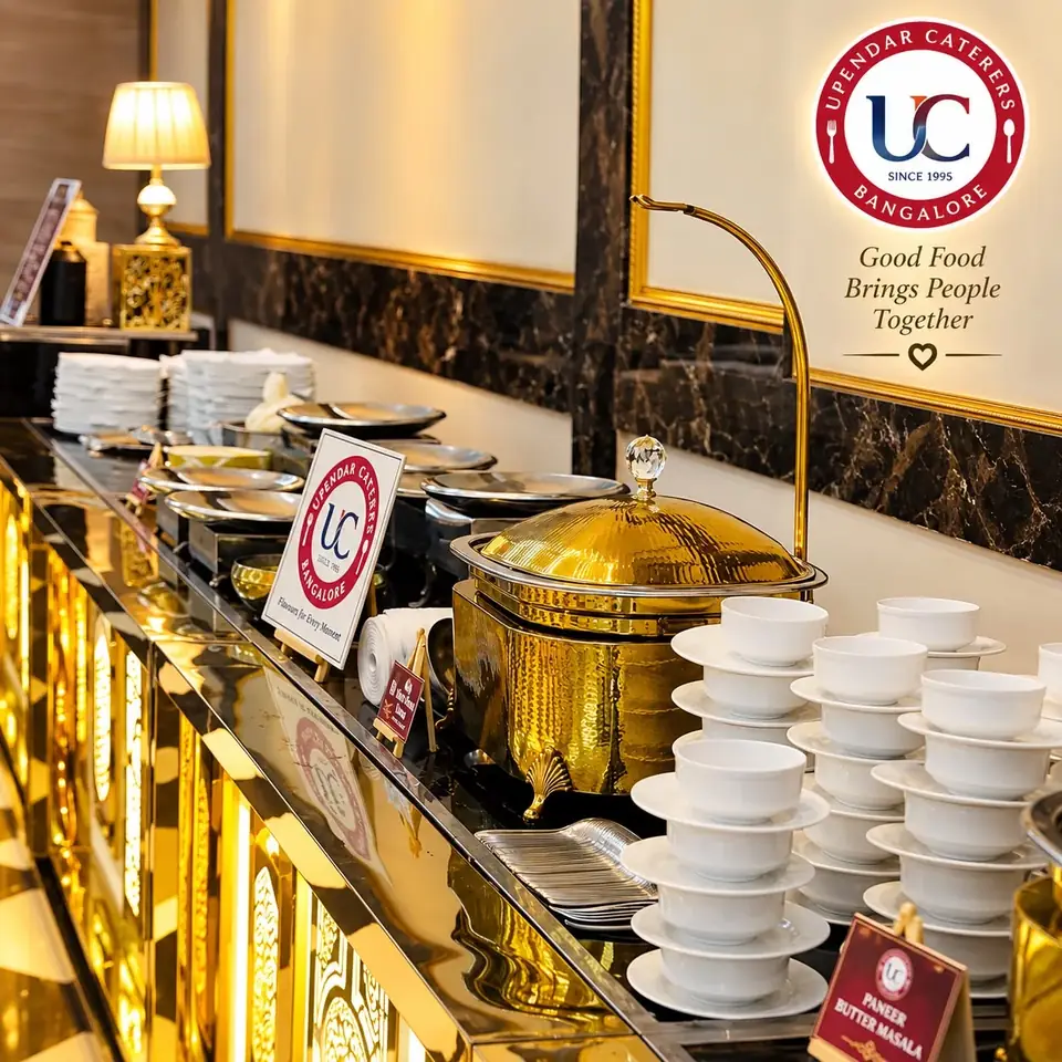 Brass serving dishes and stacks of white bowls on an indoor Upendar Caterers buffet counter